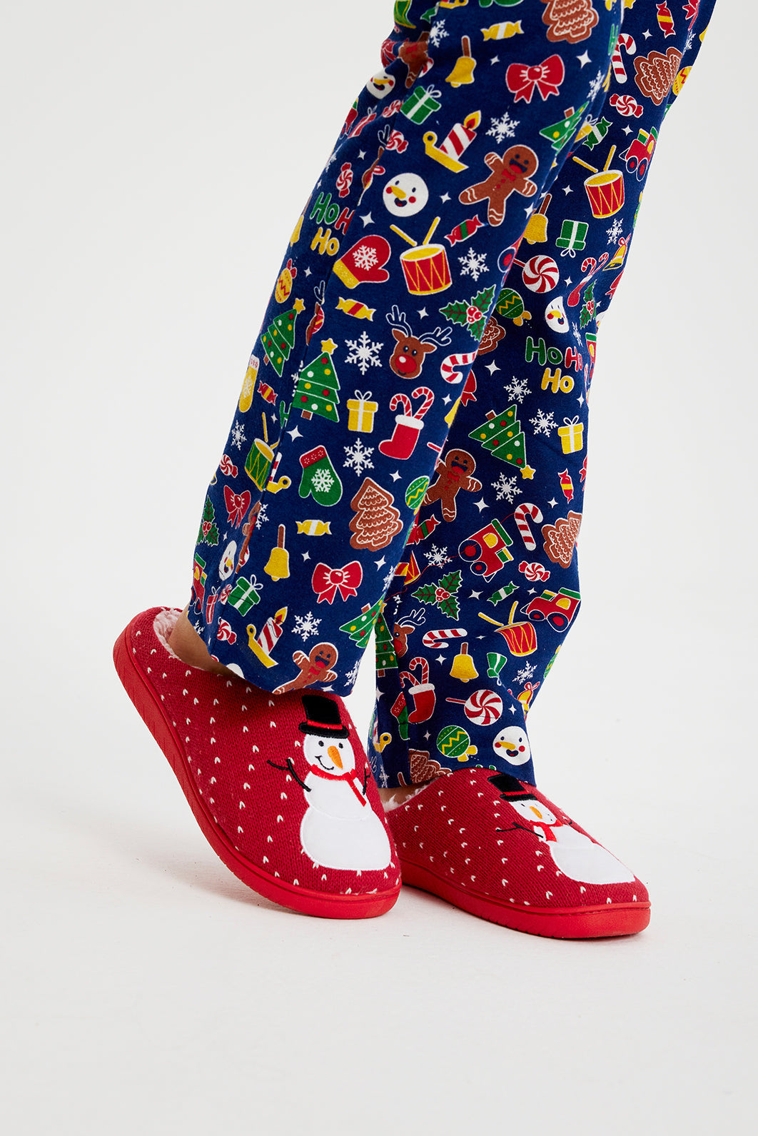 Une paire de jambes portant des chaussons de Noël rouge vif ornés d'un bonhomme de neige.